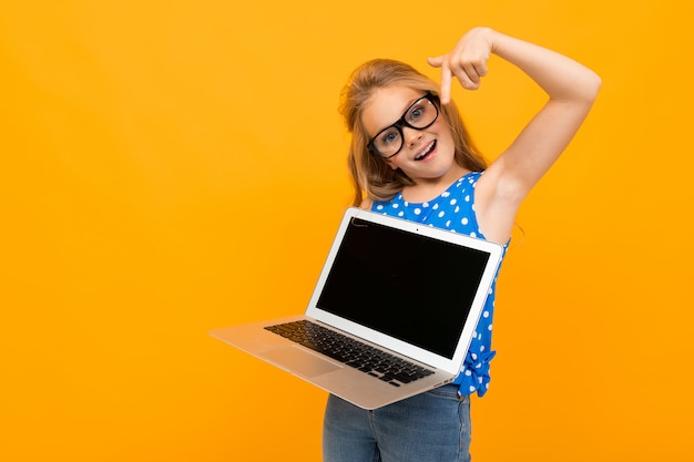 Nice little girl with her glasses holds a laptop and smiles isolated on white wall