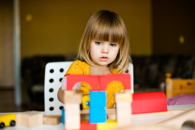 Nice little girl in the yellow dress playing with colorful bricks