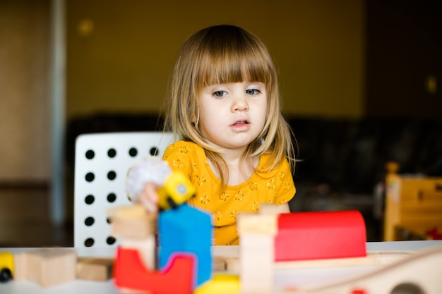 Nice little girl in the yellow dress playing with colorful bricks