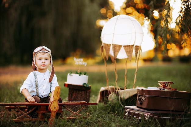 Nice little pilot boy in vintage aviator hat looking at camera while sitting on big toy wooden plane