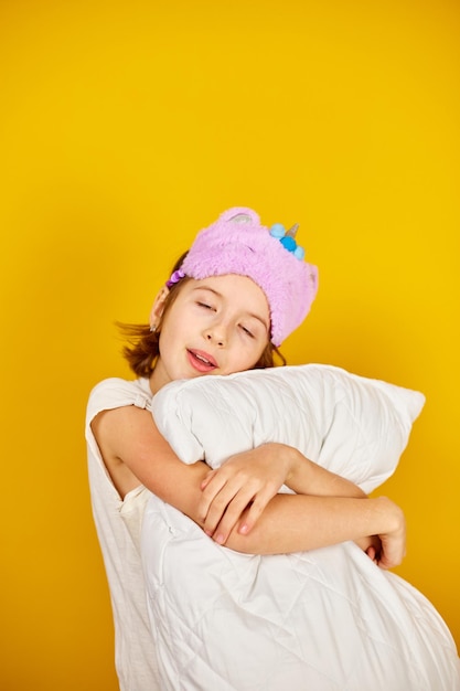 Nice teenage girl in white pyjamas with a violet sleeping mask embraces a pillow