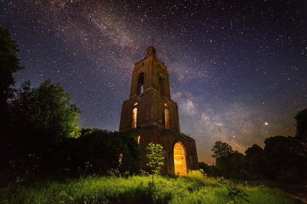 Night bell tower ruin in forest at starry night with internal light