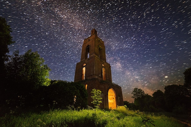 Night bell tower ruin in forest at starry night with internal light