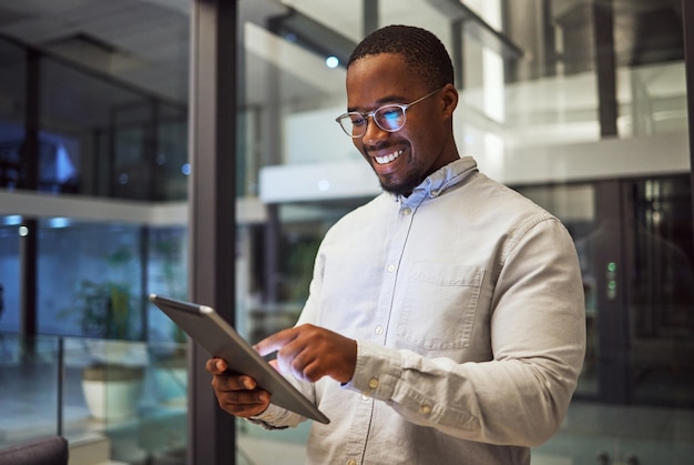 Night business tablet and black man typing and reading information online doing research and smiling at good results working late Happy male on internet for marketing strategy in Nigeria office