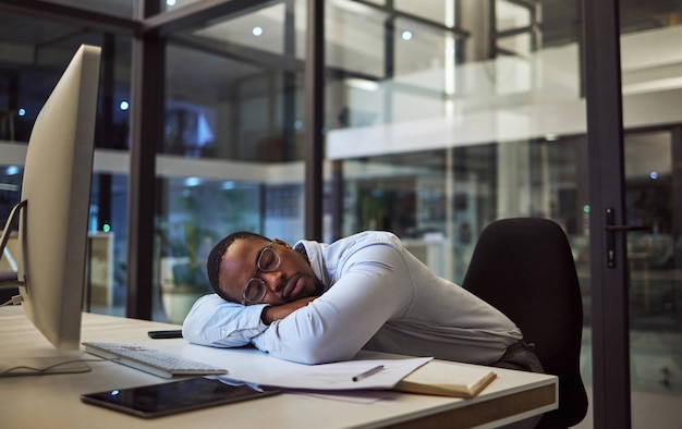 Night business work sleep and businessman sleeping at desk with computer in dark office at a corporate company Tired African manager or employee with burnout taking a nap while working overtime