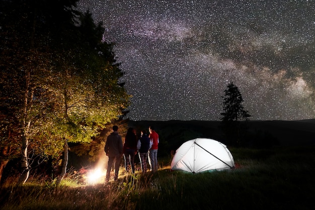 Photo night camping in the forest under a magical sky with lots of bright stars and milky way on hills.