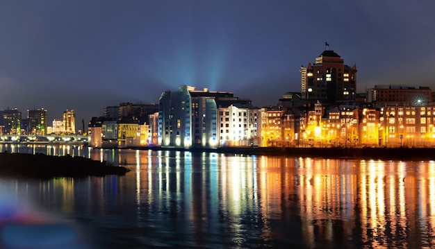 The night city stands on the river and the lights of the windows can be seen in the reflecti