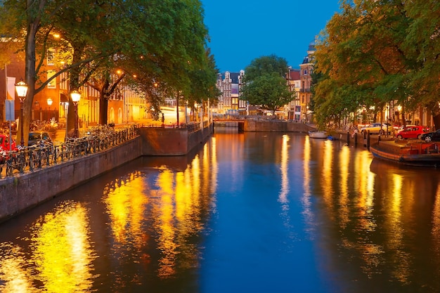 Night city view of Amsterdam canal, bridge, boats and bicycles, Holland, Netherlands.