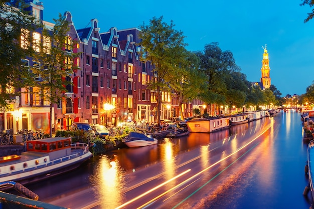 Night city view of Amsterdam canal Prinsengracht with houseboats and Westerkerk church and luminous track from the boat, Holland, Netherlands. Used toning