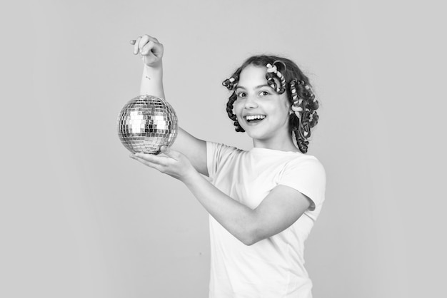 Night club Hairdresser salon Child hold golden disco ball Retro party Cheerful girl with disco ball Fashion kid posing with curlers in hair Fancy teen Hairstyle for disco party Have fun