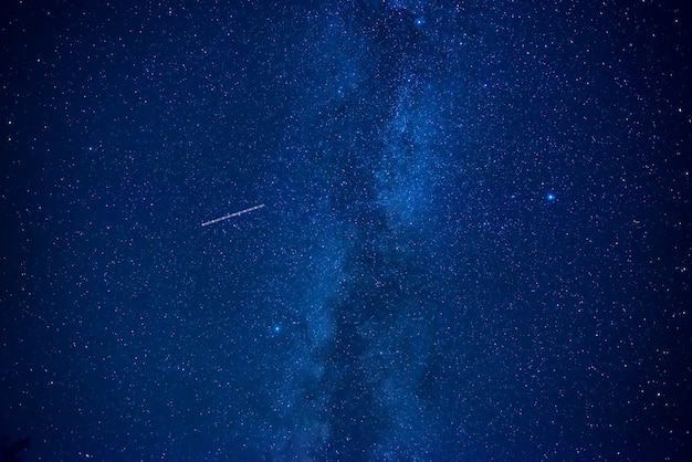 Night dark blue sky with many stars of milky way galaxy and flying satellite