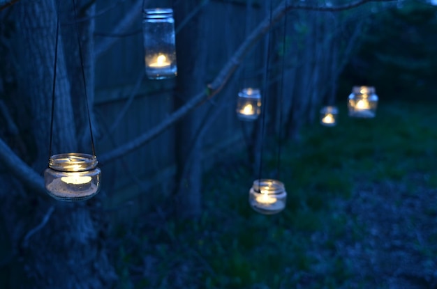 Photo night garden hand-crafted lanterns glass jars tied to tree branches with tea light candle  inside