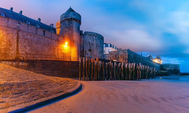 Night panoramic view at low tide of beautiful walled city Intra-Muros in Saint-Malo, also known as city corsaire, Brittany, France