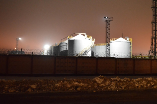 Night photo of a tank farm of a petroleum refinery a petrochemical plant through a fence