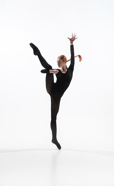 Night. Young and graceful ballet dancer in minimal black style isolated on white studio background. Art, motion, action, flexibility, inspiration concept. Flexible caucasian ballet dancer.