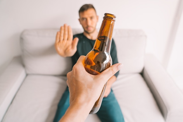 No alcohol Young man refuses to drink beer making stop gesture to bottle of beer