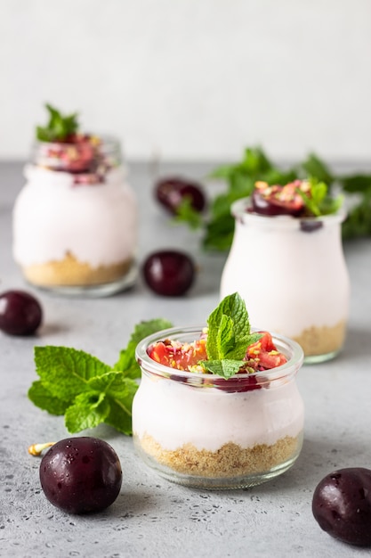 No baked cheesecake with cherry in glass jars, fresh cherries and mint on a grey stone 