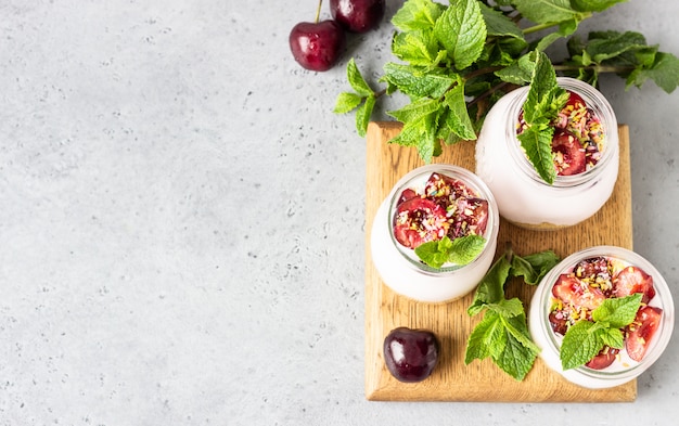 No baked cheesecake with cherry in glass jars, fresh cherries and mint on a grey stone 