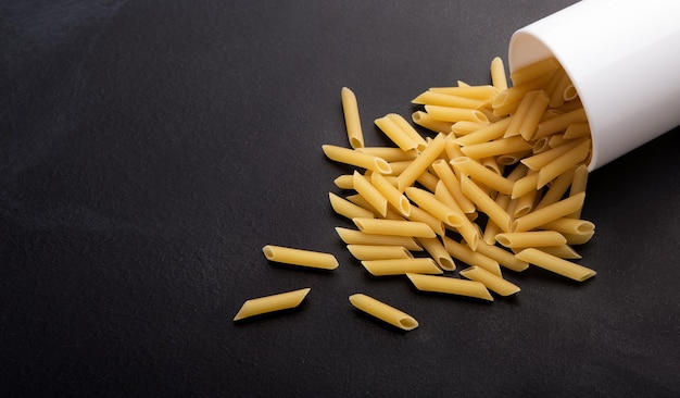 No gluten. Healthy pasta scattering from cup on black background