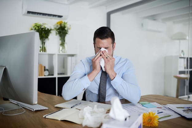 No sick days left Shot of a young businessman suffering with allergies at work