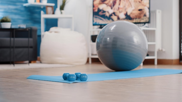 Nobody in living room with sport and workout equipment to train at home. Empty space with dumbbells used for weights lifting and fitness toning ball on floor yoga mat. Training activity