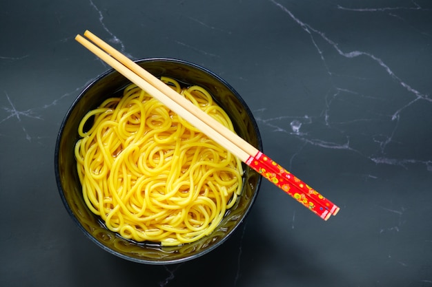 noodles are in a bowl placed on table.yellow noodle in black bowl with copy space.