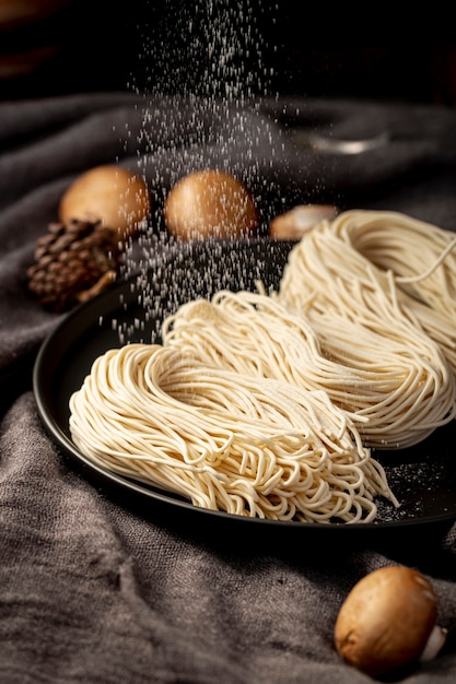 Noodles in a black plate on a grey background with mushrooms