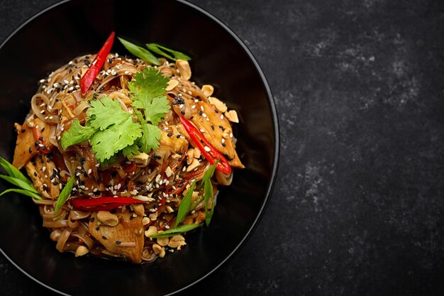 Noodles with chicken and vegetables on a black plate