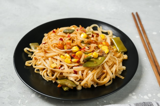 Noodles with vegetables in a black plate with soy sauce top view.