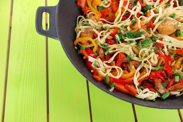 Noodles with vegetables on wok on wooden background