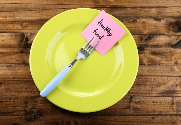 Note paper with message attached to fork on plate on color wooden background