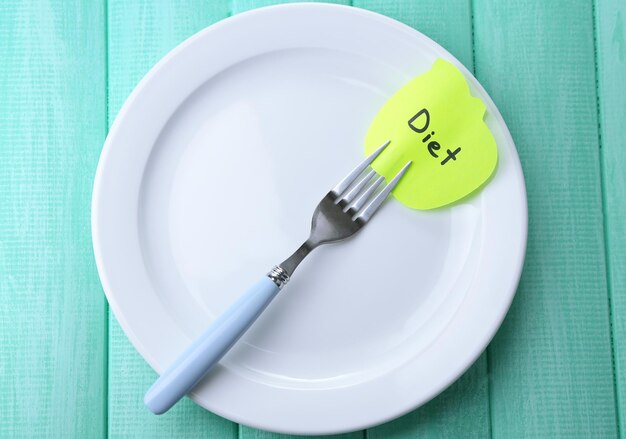 Note paper with message attached to fork on plate on color wooden background