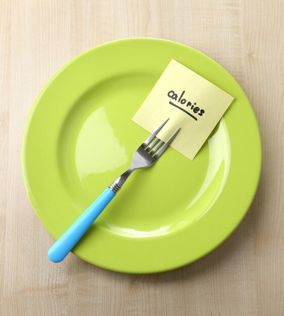 Note paper with message attached to fork on plate on wooden background