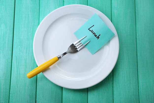 Note paper with message attached to fork on plate on wooden background