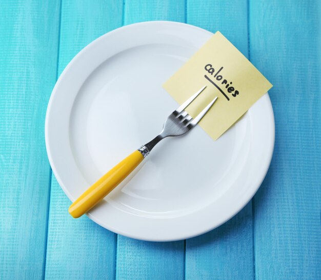 Note paper with message attached to fork on plate on wooden background