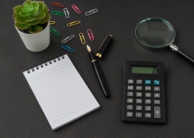 A notebook, calculator, magnifying glass and pen on black surface with a copy space. Business and finance concept.