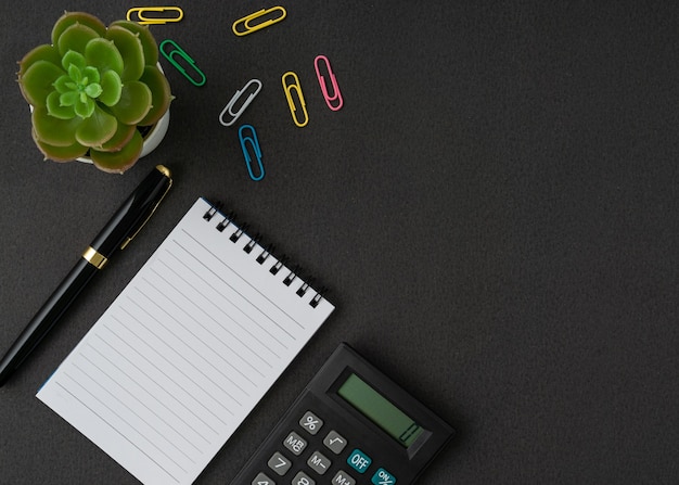 A notebook, calculator and pen on black background with a copy space. Business and finance concept. Flat lay.