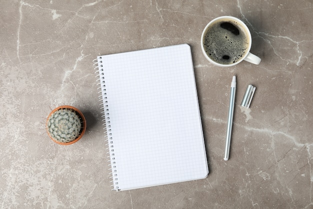 Notebook, coffee, pen and cactus on grey surface