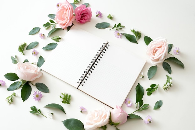 Notebook flat lay on white background with summer leaves flowers and other stationery in trendy set up style