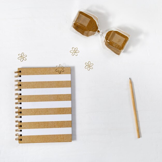 Notebook, hourglass and wooden pencil on white table