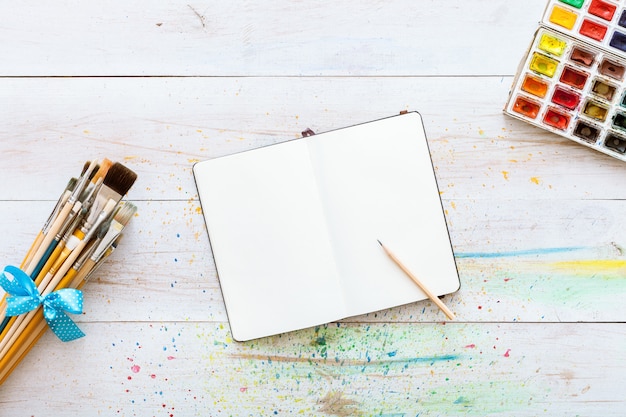 Notebook mock up with art supplies on white wooden creative table. Top view