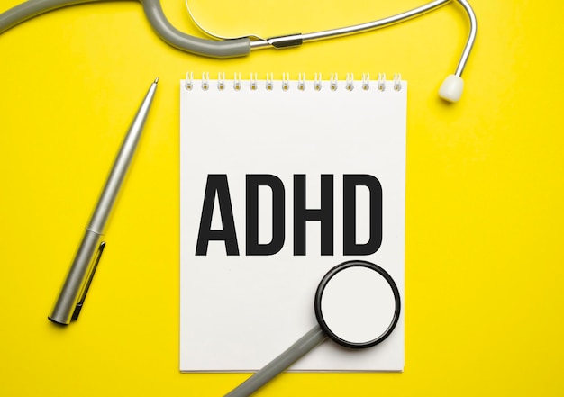 Notebook page with text ADHD Attention Deficit Hyperactivity Disorder on a table with a stethoscope and pen medical concept