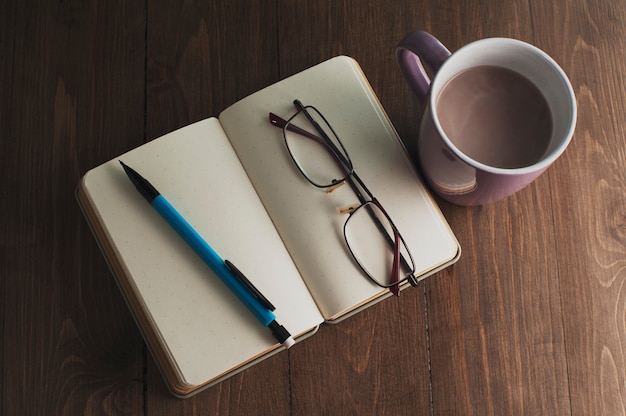 Notebook, pen, cup, glasses on a wooden table