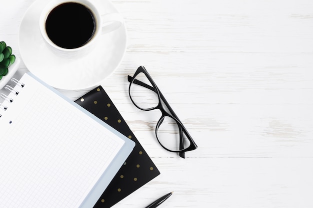 Notebook, pen, glasses, plants succulents, a cup of coffee on a white wooden table, flat lay, top view. Office table desk, workplace