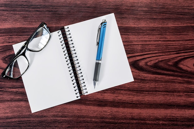 Notebook pen and reading glasses on wooden table