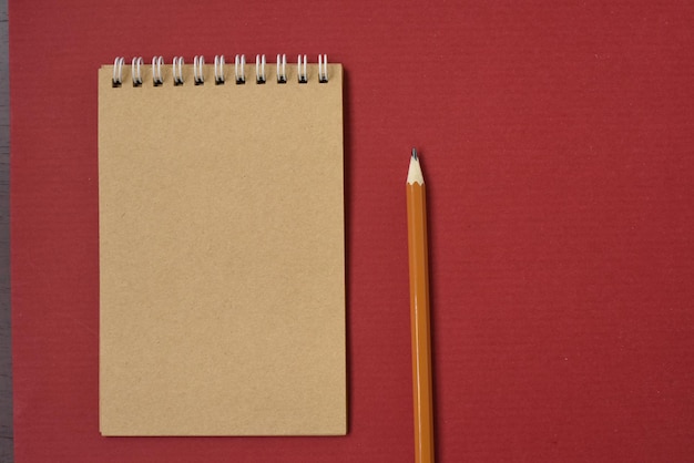 Notebook and pencil on red background