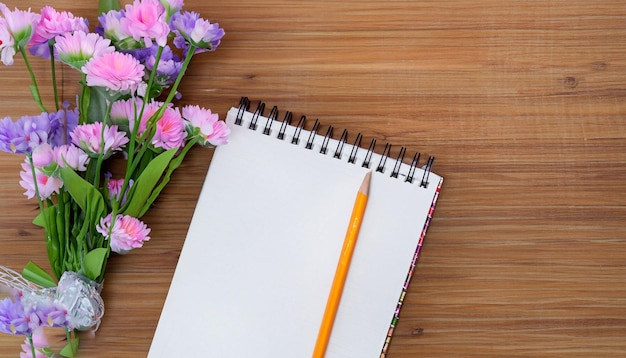 A notebook and a pencil on a wooden table with flowers.