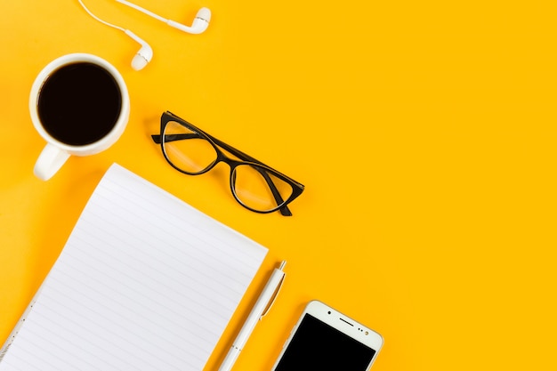 Notebook, phone, mobile, coffee, pen, glasses on a yellow background. Copy space. Top view. Flat lay