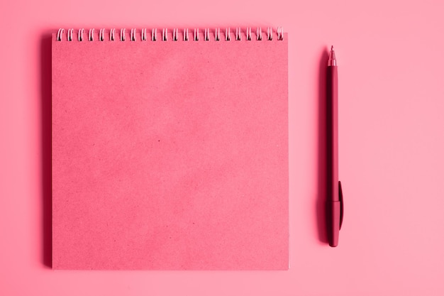 Notebook or sketchbook made of craft paper and a pen on a pink background mockup and space for text toned in viva magenta trend color of the year 2023