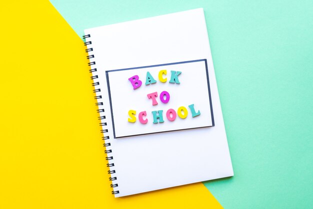 Notebook on a spiral with white sheets back to school inscription made of multicolored letters